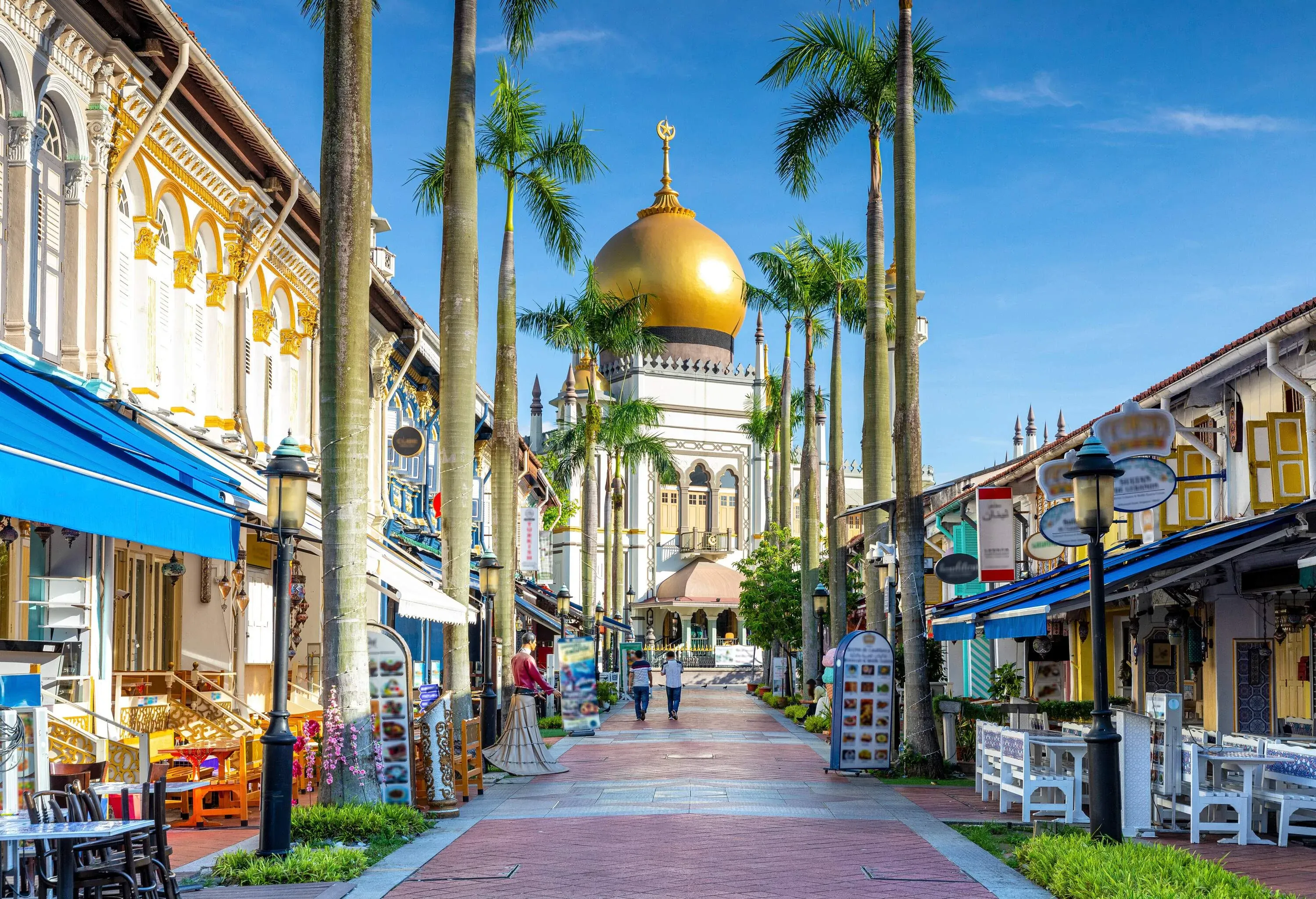An iconic roadway in the middle of shophouses framed by tall palm trees leads toward the Sultan Mosque.