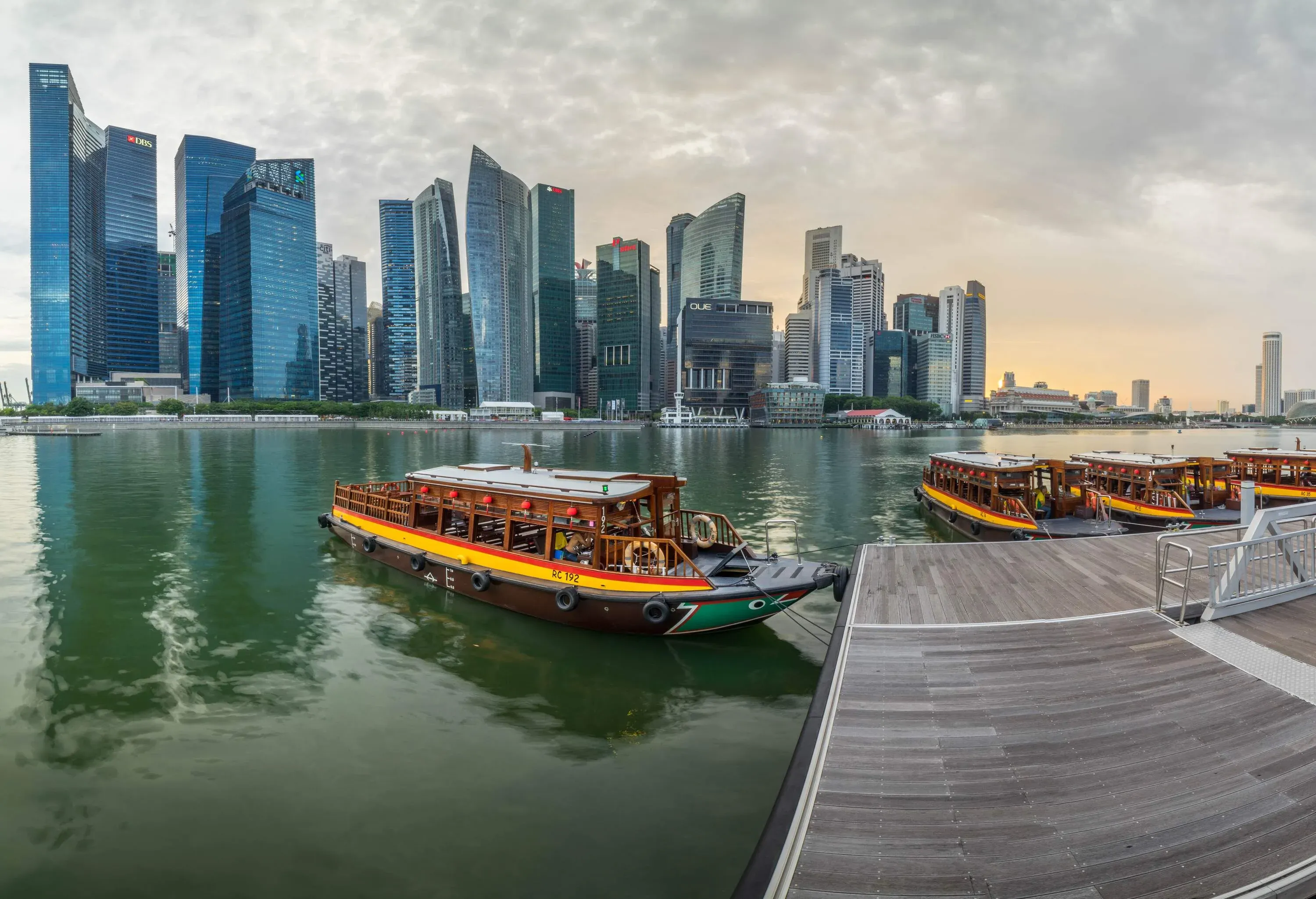 Passenger boats docked in a harbour against a backdrop of towering skyscrapers.